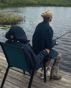 a woman sitting in a chair fishing on a lake while another person sits next to her