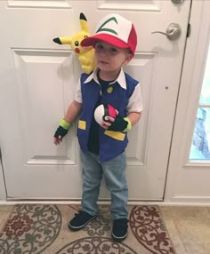 a little boy standing in front of a door wearing a hat and holding a stuffed animal