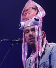 a man wearing a pink hat with an octopus on it's head while standing in front of a microphone