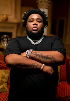 a man with his arms crossed, wearing a black t - shirt and bracelets