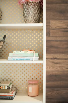 a white book shelf with some books on top of it and a vase next to it