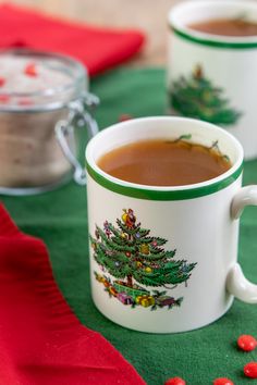 two mugs filled with hot chocolate sitting on top of a green table covered in candy