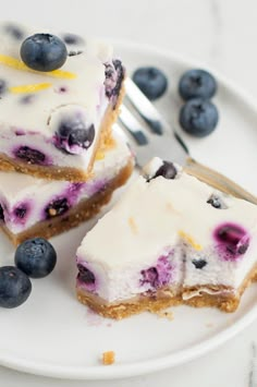 two slices of blueberry cheesecake on a white plate with silverware and fork