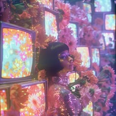 a woman standing in front of televisions with flowers around her