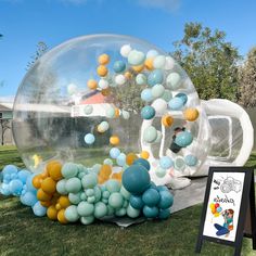 an inflatable bubble filled with blue, yellow and white balloons sitting on top of a lush green field