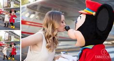 the woman is posing with mickey mouse at the airport and kissing her husband's nose