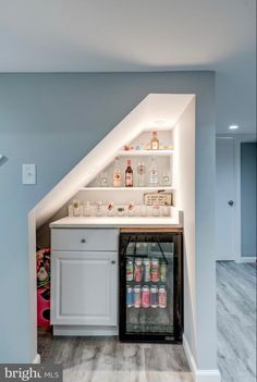 an attic kitchen with white cabinets and shelves filled with drinks