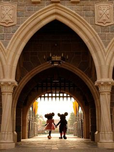 two mickey and minnie mouses holding hands under an archway