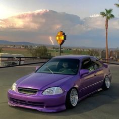 a purple car parked in a parking lot next to a street sign and palm trees