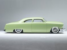 an old fashioned green car is parked in a studio area with light coming through the window