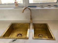 two golden sinks in front of a window