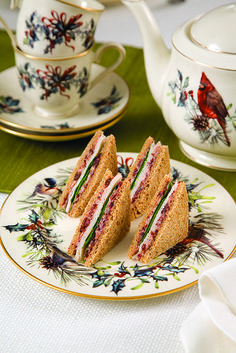 two sandwiches on plates with tea cups in the background