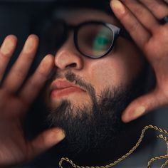 a man with glasses and a chain around his neck is staring into the distance while holding his hands to his face