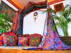 a bed covered in lots of colorful pillows and blankets next to a potted plant