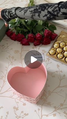 a person holding a box with chocolates in it next to roses and a heart shaped box