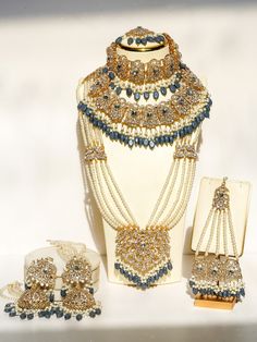 Experience the ultimate luxury with the Nazanin Gold Plated Bridal Set, a meticulously crafted 6-piece collection designed to captivate and charm. This opulent bridal set includes oversized jhumka earrings that are 4.3 inches long with attached ear chains, a resplendent choker necklace, a timeless classic necklace, a stunning long necklace, a graceful jhoomer, and a majestic maang tikka, all adorned with exquisite gold plating, shimmering white zircon stones, and captivating pantone blue beads t Blue Gray Gold, Ear Chain, Maang Tikka, Blue Bridal, Classic Necklace, Jhumka Earrings, Bridal Set, Blue Beads, Steel Blue