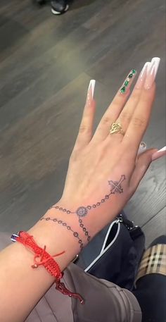 a woman's hand with tattoos on it and a red string around the wrist