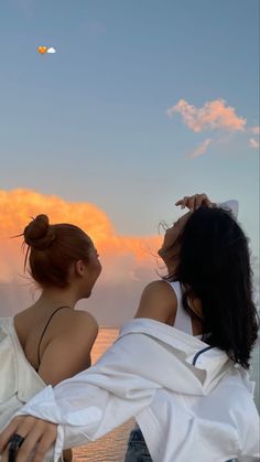 two women sitting on the back of a boat looking out at the ocean while the sun is setting