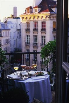 a table with food and wine on top of it in front of a balcony overlooking the city