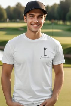 a young man wearing a white shirt and black cap smiles at the camera while standing in front of a golf course