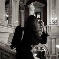 a woman in a black dress taking a photo with her cell phone at the top of stairs