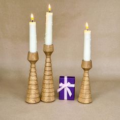 three candles are next to a purple gift box with a white bow on it and one candle is in the middle