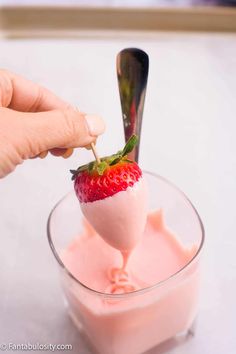 a person is dipping a strawberry into some pink yogurt with a spoon in it