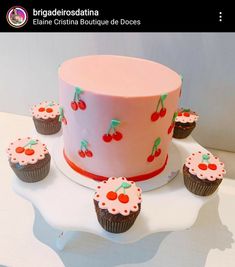 a pink cake with cherries on it and cupcakes sitting next to it