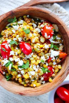 a wooden bowl filled with corn, tomatoes and feta cheese on top of a table