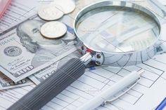 a magnifying glass sitting on top of money and paper with writing utensils