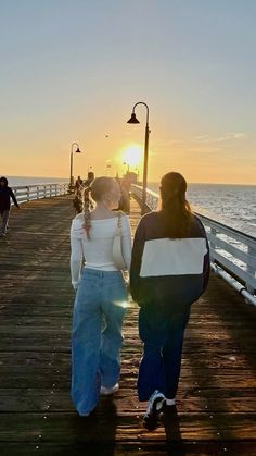 two people walking down a pier towards the ocean at sunset or sunrise, with one person carrying a shopping bag