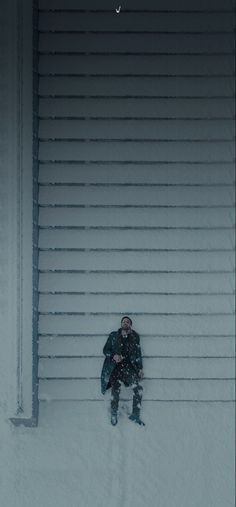 a man sitting in the snow next to a building