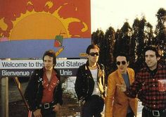 four young men standing in front of a sign with the sun on it's side