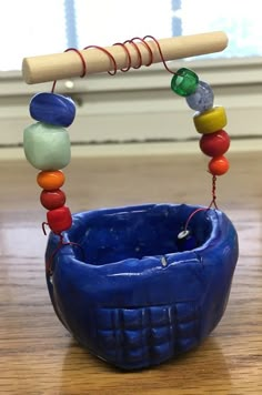 a blue bowl with beads hanging from it's side and a wooden stick in the middle