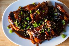 a white plate topped with meat covered in sauce and green onions on top of a wooden table