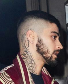 a man with a goatee and tattoos on his head looking off into the distance