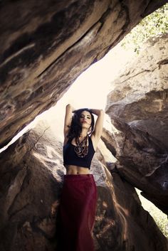 a woman standing in the middle of a cave with her hands on her head and arms behind her head