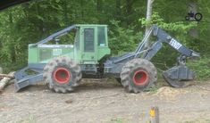 there is a large tractor that is parked in the dirt near some trees and logs