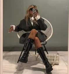 a woman sitting in a chair taking a selfie with her cell phone while wearing knee high boots