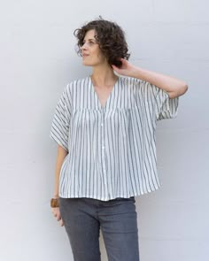 a woman standing in front of a white wall with her hand on her head and looking off to the side