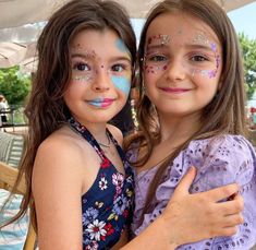 two girls with face paint hugging under an umbrella