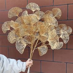 a person holding up a bunch of golden metal flowers in front of a brick wall