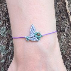 a woman's foot wearing a purple string bracelet with a green beaded bird on it