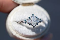 a close up of a person holding an engagement ring in their hand with blue and white diamonds on it