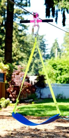 a blue and yellow swing hanging from a rope in the yard with trees in the background