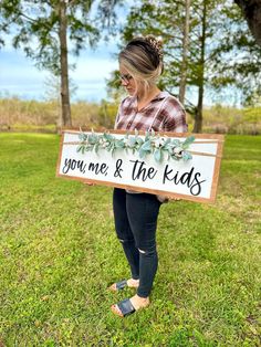 a woman standing in the grass holding a sign that says you me and the kids