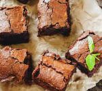 chocolate brownies on parchment paper with a sprig of green leaf next to them