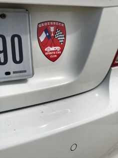 the back end of a white car with a red and blue shield on it's license plate