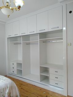 an empty bedroom with white closets and drawers on the wall next to a bed