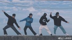 four young men jumping in the air on top of a cement wall with their arms outstretched